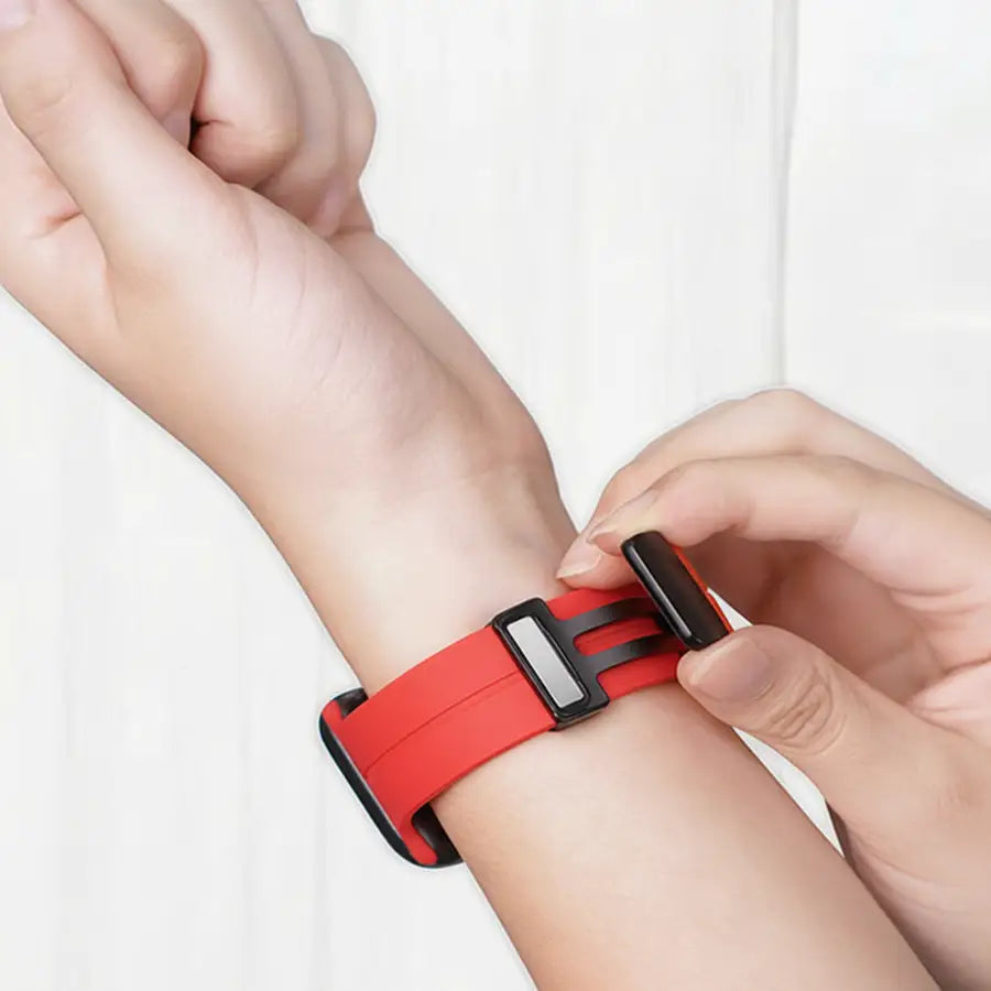 Person legt das rote Linéa Apple Watch Armband mit schwarzem Magnetverschluss am Handgelenk an.Modernes, sportliches Design aus weichem Silikon für perfekten Sitz im Alltag.